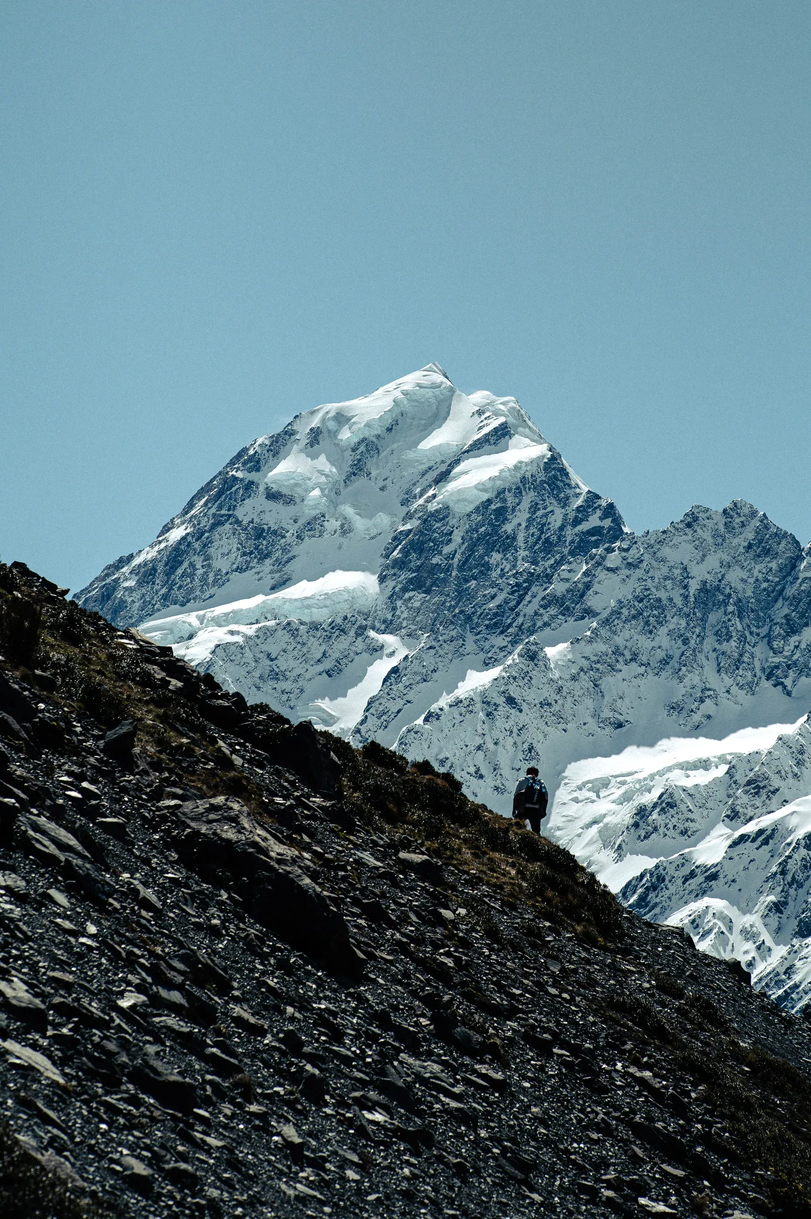 A hiker moving across an alpine ridge below snowy peaks